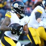 RJ Harvey nº 12 do Denver Broncos carregando a bola contra um jogador do Kansas City Chiefs.