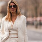 Diane Batoukina usa óculos escuros Dior marrons, um pulôver de cashmere branco com gola alta Zara, casaco e calças combinando, uma bolsa Prada marrom clara e fofa de pele sintética, luvas de couro brancas, durante uma sessão de fotos de moda de rua, em 13 de janeiro de 2025 em Paris, França.