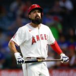 Um batedor do Los Angeles Angels, usando capacete vermelho e uniforme branco, segura um taco.