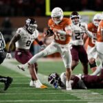 O quarterback do Texas Longhorns, Arch Manning, corre para um touchdown com um jogador do Texas A&M Aggies no chão.