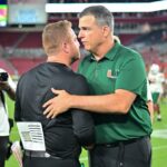 College football head coach Mario Cristobal of the Miami Hurricanes shakes hands with head coach Alex Golesh
