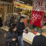 Os compradores passam por uma placa de venda em um shopping center de Melbourne.