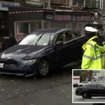 Um carro escuro danificado sendo rebocado em uma rua da cidade.