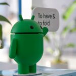 Mascote do Android 16 usando óculos escuros azuis com os braços levantados, cercado por ícones de aplicativos