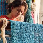 Nabil olha diretamente para a câmera, com um cachimbo na boca e na mão esquerda. Atrás dele está uma grande obra de arte em tons terrosos