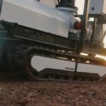 An autonomous, tracked robot sits on a dirt patch.