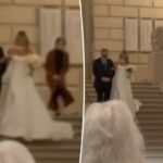 Quando a noiva começou a descer, seu coordenador de casamento pôde ser visto passando dramaticamente pelo par, deslizando pelo corrimão de pedra ao lado deles, à vista dos convidados atordoados.