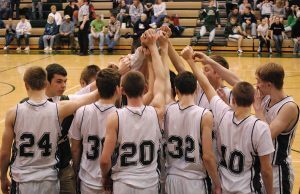 Descobriu-se que seis estudantes atletas manipularam apostas pela NCAA Time de basquete Coopersville Broncos. Um time de basquete de uma escola ou faculdade se reúne na quadra central com as mãos levantadas antes do jogo. Os jogadores vestem camisetas brancas combinando com detalhes escuros, e os espectadores sentam-se nas arquibancadas ao fundo. Descobriu-se que seis estudantes atletas manipularam apostas pela NCAA