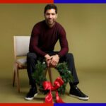 Um homem de casaco preto segurando um guarda-chuva preto olha por cima do ombro.