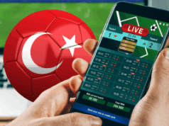 Escândalo com árbitros da liga turca faz com que mais de cem dirigentes sejam suspensos Uma pessoa segurando um smartphone exibindo uma tela de apostas esportivas ao vivo, com uma bola de futebol vermelha com a bandeira turca ao fundo, sugerindo atividades de apostas relacionadas à liga turca de futebol. Escândalo com árbitros da liga turca faz com que mais de cem dirigentes sejam suspensos