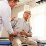 Um paciente mais velho aponta para o estômago, indicando dor para um médico.