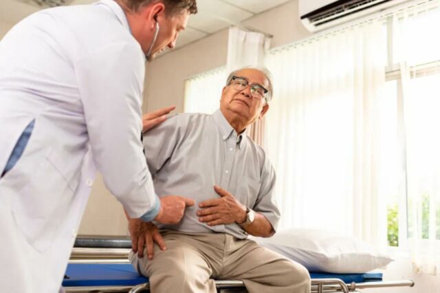 Um paciente mais velho aponta para o estômago, indicando dor para um médico.