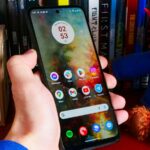 O Moto G Power (2024) deitado sobre tecido cinza e ao lado de uma estampa de flores