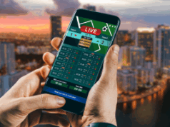 Florida House avalia revisão dos jogos de azar, endurecendo as penalidades e regulamentando os esportes de fantasia Florida House avalia revisão dos jogos de azar, endurecendo as penalidades e regulamentando os esportes de fantasia. Uma pessoa segurando um smartphone exibindo uma interface de apostas esportivas ao vivo, com o horizonte de uma cidade desfocado ao fundo ao pôr do sol.