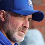 Um homem com um boné azul do New York Giants olhando para a direita.