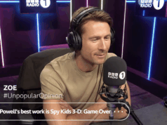 Glen Powell reagindo às opiniões impopulares de interlocutores de rádio é divertido assistir Um homem sentado em uma cabine de rádio usando fones de ouvido.
