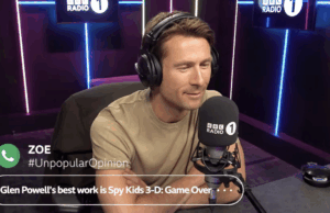 Glen Powell reagindo às opiniões impopulares de interlocutores de rádio é divertido assistir Um homem sentado em uma cabine de rádio usando fones de ouvido.