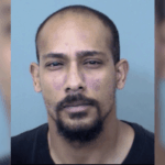 O golpista do Arizona pega 87 meses por fraude de US$ 5,6 milhões no pagamento de jogos de azar e estilo de vida. Foto de um homem adulto com cabeça raspada e cavanhaque curto, olhando diretamente para a câmera contra um fundo azul claro liso.