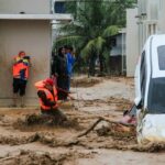 Um homem carrega seu filho enquanto atravessa as enchentes após fortes chuvas em uma área residencial de Darul Imarah, nos arredores de Banda Aceh, em 27 de novembro de 2025. (Foto de CHAIDEER MAHYUDDIN / AFP)