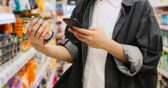 Estudante chinês asiático olhando para smartphone enquanto escolhe itens no supermercado.