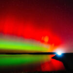 Um carro cruza a represa Hulah sob o brilho da aurora boreal em 11 de novembro de 2025, durante um raro avistamento de aurora no norte de Oklahoma.