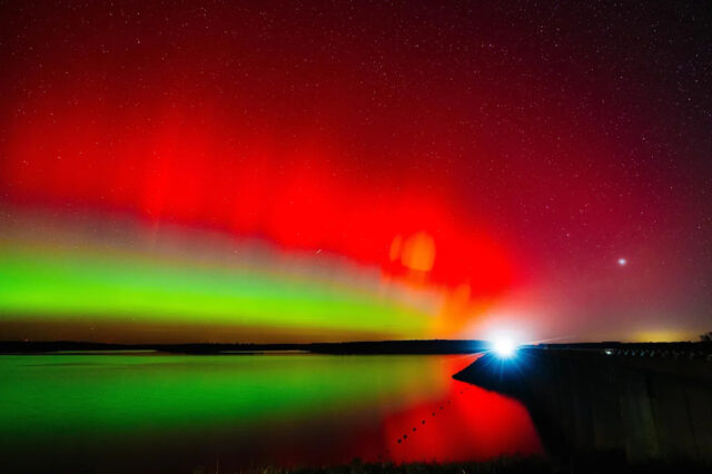 Um carro cruza a represa Hulah sob o brilho da aurora boreal em 11 de novembro de 2025, durante um raro avistamento de aurora no norte de Oklahoma.