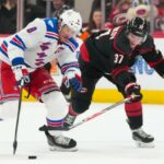 JT Miller patina com o disco passando por Andrei Svechnikov durante o segundo período da vitória do Rangers por 4 a 2 sobre os Hurricanes em 26 de novembro de 2025.