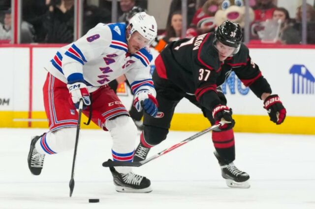 JT Miller patina com o disco passando por Andrei Svechnikov durante o segundo período da vitória do Rangers por 4 a 2 sobre os Hurricanes em 26 de novembro de 2025.
