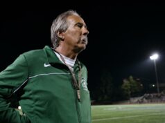 John Beam, lendário treinador de ‘Last Chance U’ da Netflix, morto após levar um tiro na cabeça John Beam, com uma jaqueta verde, olhando para um campo de futebol à noite.
