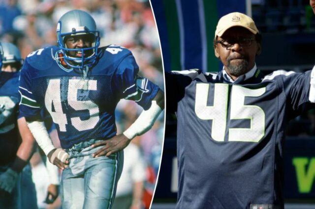 Kenny Easley, segurança do Hall da Fama do Futebol Profissional, Kenny Easley, vestindo uma camisa do Seattle Seahawks com o número 45, levanta os braços em comemoração.