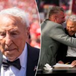 O analista da ESPN Lee Corso vestindo terno preto e gravata borboleta, com distintivo de lapela com bandeira americana, deixando o campo após sua escolha final.