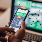 IGSA planeja estrutura de melhores práticas de IA para orientar os reguladores de jogos de azar. Uma pessoa usando um smartphone para acessar uma plataforma de apostas esportivas ao vivo, com a tela de um laptop exibindo conteúdo de apostas semelhante em segundo plano. Uma sobreposição de rede digital simboliza a inteligência artificial e as conexões de dados na indústria de jogos de azar. Mais de 5 milhões de pessoas querem parar de jogar, mostra novo estudo