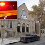 Uma sinagoga de pedra com texto hebraico acima de suas três entradas em arco, um grande vitral redondo e uma rua com carros estacionados na frente.