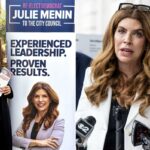 Julie Menin fala em um pódio com microfones, ladeada por um homem de terno e outros indivíduos, defendendo o Fundo para as Vítimas do 11 de Setembro.