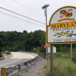 Lado de uma estrada que faz uma curva para a esquerda, com uma placa no lado direito que diz 'Maryland lhe dá as boas-vindas, aproveite sua visita!' Maryland se torna o último estado a alertar os licenciados sobre mercados de previsão