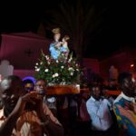 Uma multidão carrega uma estátua da Virgem Maria em uma praça, com um mural representando Claudia Cardinale na parede