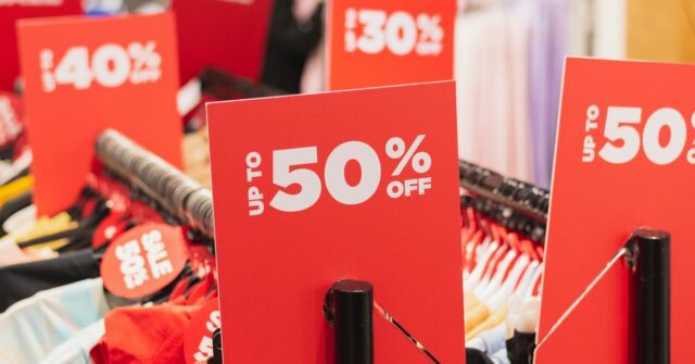 Negócios duvidosos abundam nas vendas da Black Friday – veja Sinais de desconto vermelhos em cabideiros em uma loja de roupas.