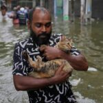 Um homem atravessa uma estrada inundada carregando um gato em Colombo, Sri Lanka, sábado, 29 de novembro de 2025. (AP Photo/Eranga Jayawardena)