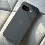 O Google Pixel 9a em pé em um parque, com a parte traseira roxa voltada para a câmera.