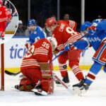 O pivô do New York Rangers, Noah Laba, chuta o disco para ultrapassar o goleiro do Detroit Red Wings, Cam Talbot.