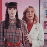 Mulher branca com jaleco branco ao lado de uma American Girl Doll em tamanho real