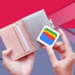 Uma mão segurando o logotipo da Carteira virtual do Google contra um fundo colorido com listras azuis, vermelhas, amarelas e verdes exclusivas do Google