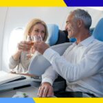 Uma área de estar moderna com assentos cinza e rosa, luzes circulares suspensas e uma parede texturizada.