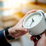 Mão masculina ajustando um despertador branco, ilustrando o gerenciamento do tempo.