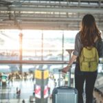 Viajante feminina com mochila e bagagem olhando pela janela de um aeroporto.