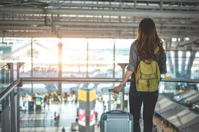 Os estados mais perigosos dos EUA para viajantes individuais revelados Viajante feminina com mochila e bagagem olhando pela janela de um aeroporto.