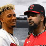 Os jogadores da MLB Emmanuel Clase e Luis Ortiz acusados ​​de apostas esportivas e conspiração para lavagem de dinheiro. Dois jogadores de beisebol em frente a um campo de beisebol. O jogador da esquerda tem cabelos loiros curtos e cacheados e sorri enquanto veste uma camisa branca e uma corrente dourada. O jogador da direita tem longas tranças escuras, barba e veste uma camisa de beisebol vermelha e um boné preto com um 'C' vermelho. O fundo mostra um campo de beisebol em tons de cinza e luzes do estádio.