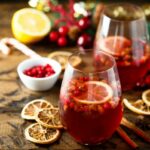 Dois copos de ponche caseiro com especiarias e frutas em uma mesa de madeira.