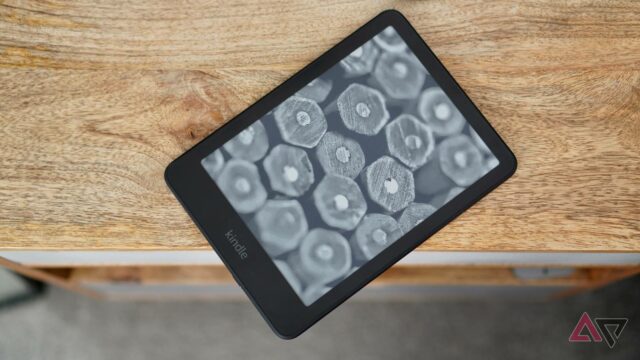 Kindle Paperwhite (2024) deitado na borda da mesa mostrando uma tela com seleção de livros