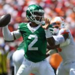 Jogador nº 2 do New York Jets no chão, com um jogador do Carolina Panthers também no chão à sua frente.